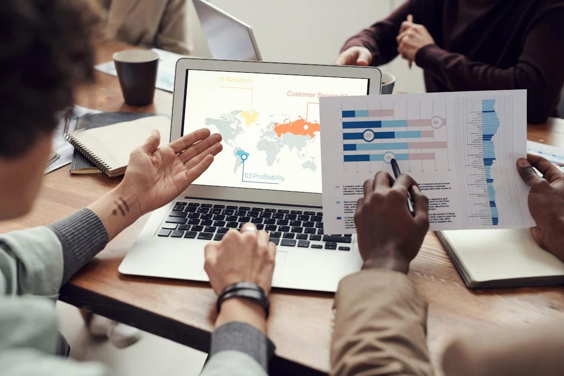 Two people reviewing a paper alongside maps on a laptop screen