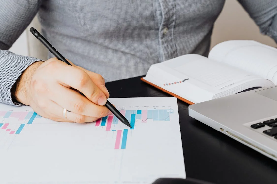 A person pointing to graphs on paper with a pen