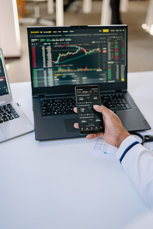 an individual navigating financial data on their phone and computer at the same time